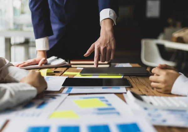 Team meeting with people reviewing charts and reports while one person points at a laptop